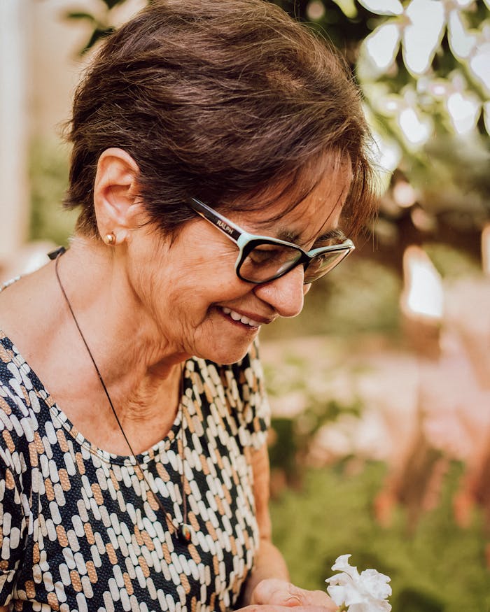Elderly woman smiling outdoors wearing glasses showcasing joy and contentment.