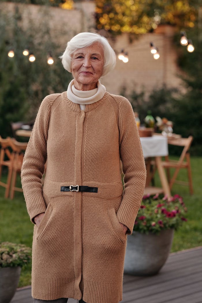 Cheerful senior lady with gray hair smiling and looking at camera in backyard with garlands